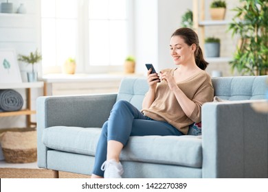 Happy casual beautiful woman is talking on a phone sitting on a sofa at home.