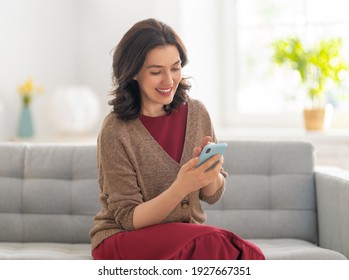 Happy Casual Beautiful Woman Is Using A Phone Sitting On A Sofa At Home.