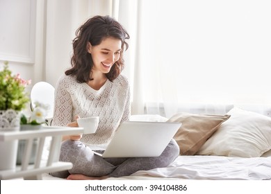 Happy casual beautiful woman working on a laptop sitting on the bed in the house. - Shutterstock ID 394104886