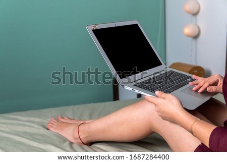 Happy casual beautiful woman working on a laptop sitting on the bed in the house. top view