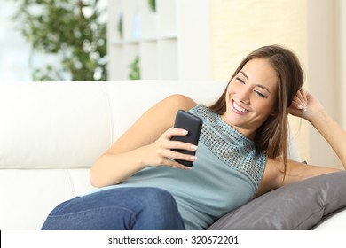 Happy Casual Housewife Using A Mobile Phone Sitting On A Couch At Home