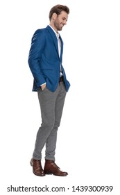Happy casual man holding his hand in his pockets and smiling while looking down and wearing a suit, posing on white studio background