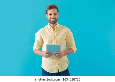 Happy Casual Man Holding A Tablet And Looking Forward While Smiling And Standing On Blue Studio Background