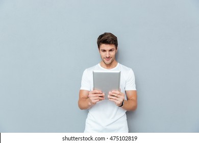 Happy Casual Man Using Tablet Computer Isolated On A Gray Background