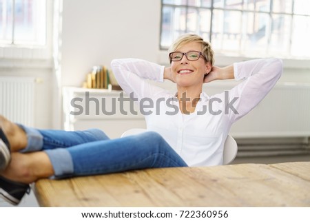 Happy casual young woman relaxing at home with her feet on the table and eyes closed with a beaming smile
