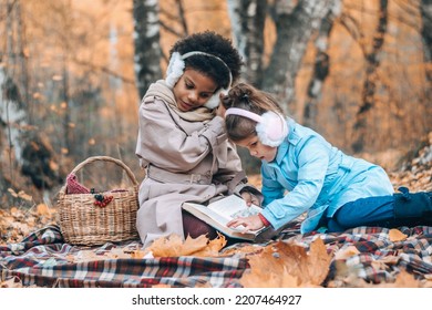 Happy Caucasian and African-American girls read a book together at a picnic in the autumn park.Diverse people,autumn concept. - Shutterstock ID 2207464927