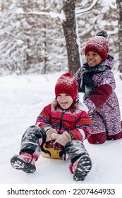 Happy Caucasian and African-American girls ride a saucer in the winter park.Beautiful trees are covered with white snow.Winter fun,active lifestyle concept. - Shutterstock ID 2207464933