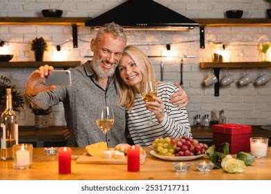 Happy caucasian aged couple taking selfie using mobile phone on a romantic date in the kitchen. Celebration of special event, anniversary, engagement, proposal online on vlog blog - Powered by Shutterstock