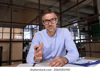 Happy caucasian businessman in glasses talking to camera at work by video call conference. Financial advisor executive consulting client remotely online in modern office looking at camera. Webcam view