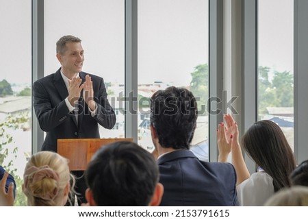 Happy caucasian businessman stand clapping hands on podium for celebration with other participants in seminar event. Selective focus.