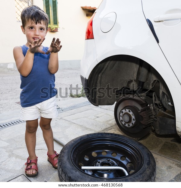 Happy caucasian child fixing the\
car changing the wheel alone outdoor, showing his dirty\
hands