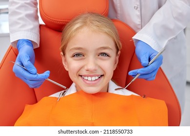 Happy Caucasian Child Girl Came To See The Dentist. Kid Sits In Dental Chair. Cropped Dentist Bent Over Her, Top View. Happy Patient And Dentist Concept. Adorable Child Look At Camers Smiling