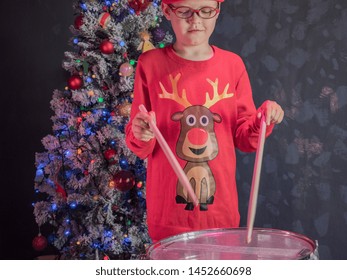 Happy Caucasian childish drummer in carnival costume Santa Claus Deer plays on a new drum set with drum sticks in his hands. Parents bought child drum as gift for Christmas. Lights on Christmas tree - Shutterstock ID 1452660698
