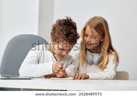 Happy Caucasian children studying at home with their laptops and headphones, immersed in online education The brother and sister are sitting at a table in their cozy living room, focused and connected