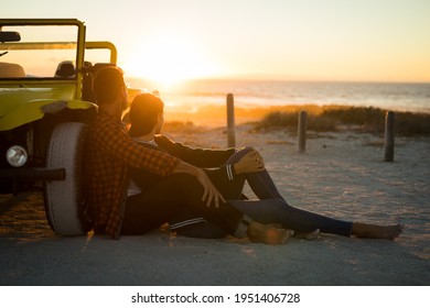 Happy caucasian couple leaning against beach buggy by the sea watching sunset. beach break on summer holiday road trip.