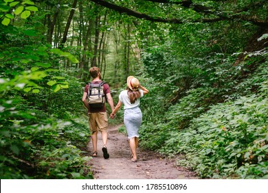 Happy caucasian couple are walking in a dense forest along the path holding hands, rear view. Hikers with backpack looking for place for picnic in wooded area in the summer. Walk outdoors together. - Powered by Shutterstock