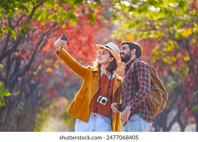 Happy caucasian couple are walking together in public park during autumn with maple and beech tree while taking selfie for fall color travel destination and family happiness - Powered by Shutterstock