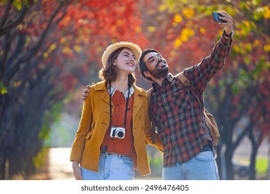 Happy caucasian couple are walking together in the public park during autumn with maple and beech tree while taking selfie for fall color travel destination and family happiness - Powered by Shutterstock