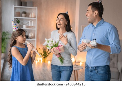 Happy caucasian family celebrating mother's birthday wearing party hats. Man husband with little preteen teenager daughter girl playing on musical instruments guitar ukulele flute and sing a song - Powered by Shutterstock