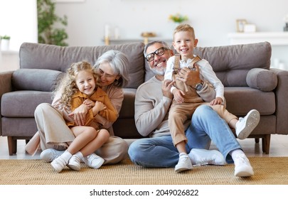 Happy caucasian family grandparents and two cute little kids brother and sister sitting on floor in living room and hugging embracing, looking at camera with smile while spending great time together - Powered by Shutterstock