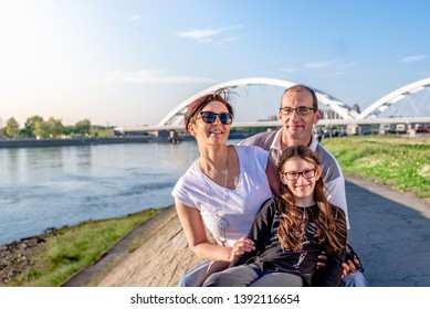 Happy Caucasian Family Of Three Spending Time Together On The River Quay. Wearing Glasses, Smiling And Looking At Camera. 