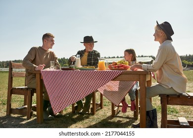 Happy Caucasian Farming Family Having Lunch With Fresh Organic Products In Countryside Outdoors. Grandparents And Grandchildren Spending Time Together. Modern Farm Lifestyle. Sunny Day