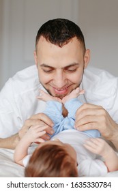 Happy Caucasian Father Holding Newborn Baby. Male Bearded Man Parent Hugging Kissing His Child Daughter Son Feet. Authentic Lifestyle Candid Moment. Proud Young Dad. Family Fathers Day.