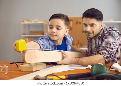 Happy Caucasian Father And Son Together Make Wooden Birdhouse At Home Workshop. Cheerful Dad And Boy Child Measuring Wood Plank With Tape Ruler. Woodworking Craft Work Family Hobby And Parenthood