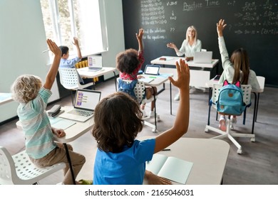 Happy Caucasian female teacher having maths lesson with elementary diverse schoolchildren sitting at desk using laptops. Full class of kids raising hands knowing answer to task written on chalkboard. - Powered by Shutterstock