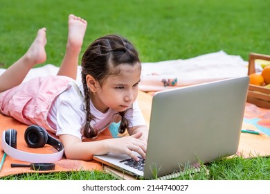 Happy Caucasian girl child smiling, looking and using at laptop computer in park. Learning online education concept.
