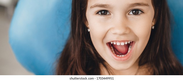 Happy caucasian girl with opened mouth smiling at camera after a teeth examination at the pediatric dentist