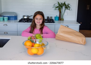 Happy Caucasian Girl Unpacking Groceries In Kitchen. Childhood, Leisure And Spending Free Time At Home.