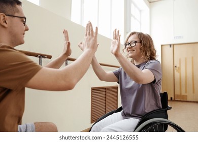 Happy Caucasian girl in wheelchair and young man doing double five after dance practice - Powered by Shutterstock