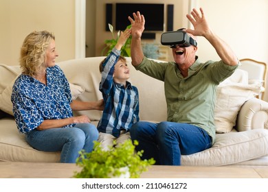 Happy caucasian grandmother and grandson watching grandfather wearing vr headset on couch at home. virtual reality and futuristic technology concept, unaltered. - Powered by Shutterstock