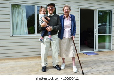 Happy Caucasian Grandparents Holding Their Granddaughter Outside Their Retirement Home.Concept Photo Of Grandparents, Grandchild, Childhood,relationship, Lifestyle, Family. Real People. Copy Space