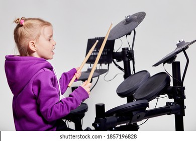 Happy Caucasian Kid Girl Drummer. Girl Playing On Elettronic Drum Kit Or Learns To Play Drums In Music School. Emotional Portrait. Mock Up, Studio On Gray Background. Free Space For Advertisement.