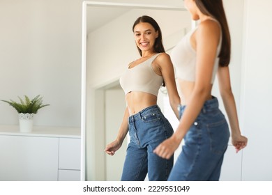 Happy caucasian lady enjoying her reflection in mirror, posing after successful weight loss and smiling, standing near mirror at home. Slimming and dieting concept - Powered by Shutterstock