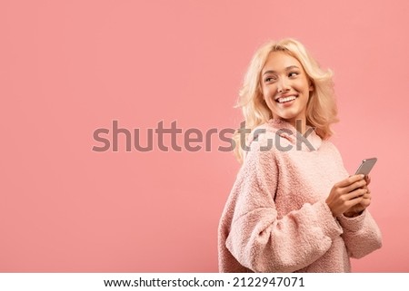 Happy caucasian lady with newest smartphone looking back at free space over pink studio background, panorama. Stylish woman using entertaining mobile application on cellphone