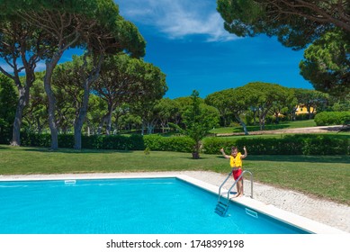 Happy Caucasian Little Boy In Yellow Life Jacket Entering Swimming Pool. Golf Course At The Background. Golf Club With Green Grass. Family Vacation Concept.