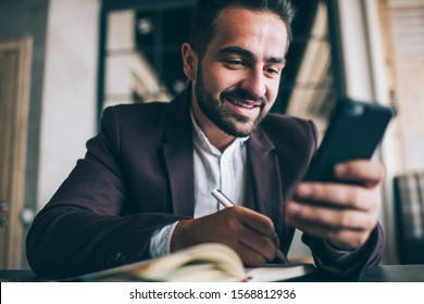 Happy Caucasian Male Entrepreneur Using Mobile Phone For Searching Information Making Notes, Positive Prosperous Businessman Satisfied With New App On Smartphone For Banking And Transactions