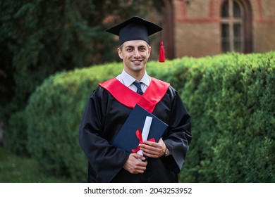 Happy Caucasian Male Graduate In Graduation Glow With Diploma Looking At Camera In Campus.