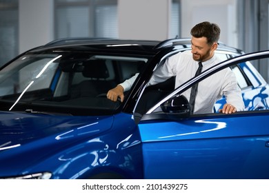 Happy caucasian man in formal wear getting inside luxury modern car for testing interior before purchase. Concept of dealership, selling and purchase.