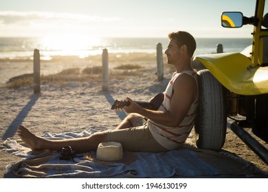 Happy caucasian man leaning against beach buggy by the sea playing guitar. beach break on summer holiday road trip. - Powered by Shutterstock