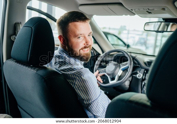 Happy caucasian man sitting inside\
new crossover car and checking all function of new model at\
showroom. Male customer examining various auto at modern\
salon.