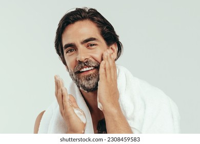 Happy caucasian man takes pride in his grooming routine, carefully applying shaving cream to his beard. With a steady hand and a focused gaze, he prepares his face for a close shave in a studio. - Powered by Shutterstock