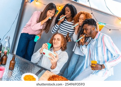 Happy caucasian man taking selfie while friends blowing streamers during birthday rooftop party - Powered by Shutterstock