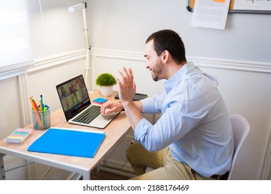 Happy Caucasian Man Waving Hello On An Online Meeting Or Video Call While Working From Home