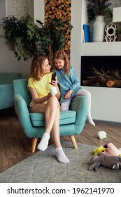 Happy Caucasian Mom Is Sitting In A Chair With Her Daughter And Watching Something Funny On A Phone