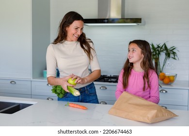 Happy Caucasian Mother And Daughter Unpacking Groceries In Kitchen. Family Time, Having Fun Together At Home.