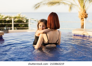 Happy Caucasian Mother And Her Little Cute Daughter Playing In Swimming Pool. Mother And Baby Girl Swim In The Pool. Mom Holding Her Daughter In Her Arms In The Pool And Teaching Her To Swim